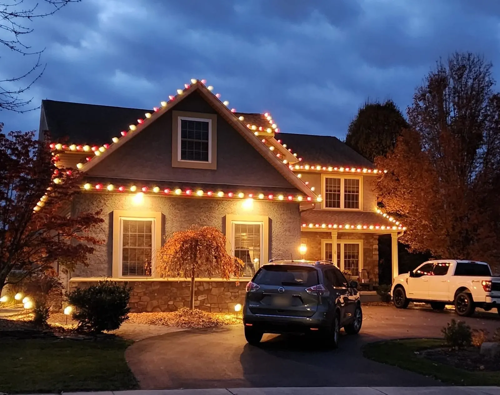 SZNS holiday lighting installation with alternating red and warm-white C9 bulbs outlining the gables of a stucco and stone home in Forks Township, PA, at dusk.