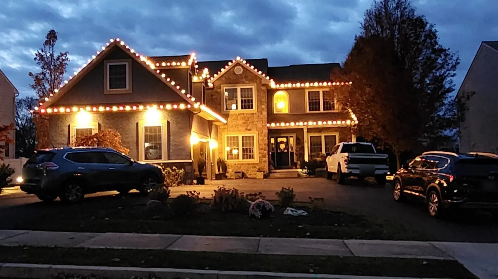 Street view of a two-story stucco and stone home in Forks Township, PA, with red and warm-white C9 lights along every roofline, installed by SZNS.